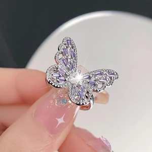Macro detail of a silver butterfly ring with purple zircon gemstones on a finger