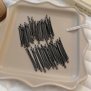Détail macro de pinces à cheveux ondulées en métal noir sur un plateau élégant