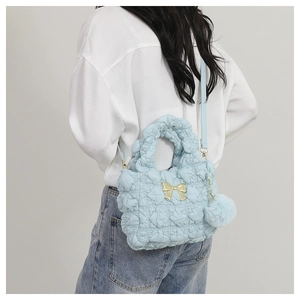 Detail of light blue pleated cloud bag with golden bow and plush pendant on model