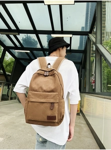 Brown canvas backpack with leather zip pulls shown in a casual lifestyle outdoor setting