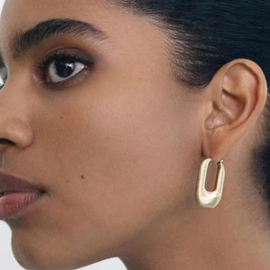 Gros plan d'un mannequin portant une boucle d'oreille en U texturée en or 18 carats