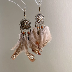 Detailed close-up of dreamcatcher earrings with bronze discs, brown beads and feathers