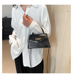 Détail d'un mini sac carré noir en cuir avec boucle nœud dorée et bandoulière élégante