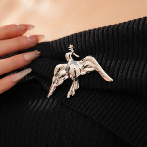 Macro shot of silver bird brooch with olive branch on black knitted fabric background