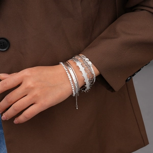 Detail view of seven-piece silver geometric bracelet set worn with a brown blazer