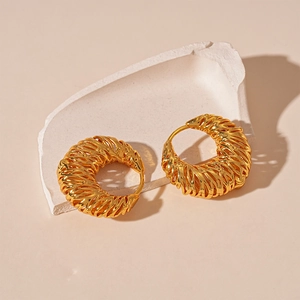Golden woven hollow geometric C-shaped hoop earrings on white stone display