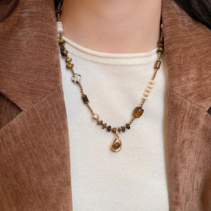 Detail of tiger eye bead necklace with gold drop pendant worn over brown corduroy jacket