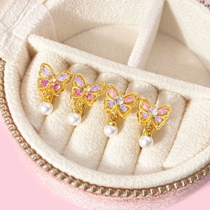 Détails de boucles d'oreilles papillon avec zircons roses et perles dans un coffret