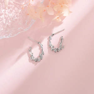 Makroaufnahme der silbernen Olivenzweig-Ohrringe aus 925 Sterling Silber auf rosa Hintergrund