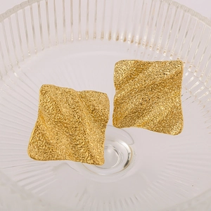 Golden titanium steel square earrings with textured finish in a glass bowl