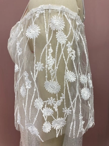 Macro shot of delicate white floral lace embroidery and sheer mesh fabric on wedding gown