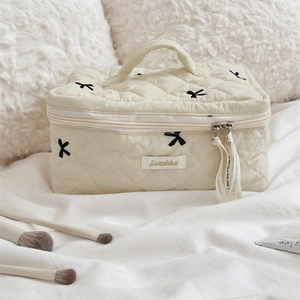 Close-up of beige quilted cotton makeup bag with black bow embroidery and brushes