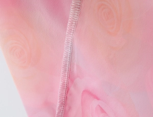 Detail of pink floral chiffon fabric showing delicate rose print and white overlock stitching