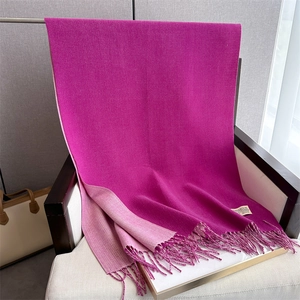 Detail of a pink cashmere-like scarf draped over a chair showing tassels and texture