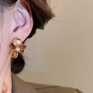 Detail of 18k gold flower earring with brown enamel and pearl on model ear