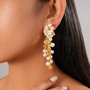 Elegant gold flower drop earrings with white pearls and sparkling rhinestones on model