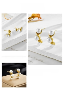 Detail of gold metal earrings with three white pearls in a curved minimalist design