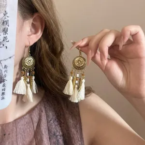 Détail de boucles d'oreilles bohèmes à pompons avec motif floral rétro et plumes