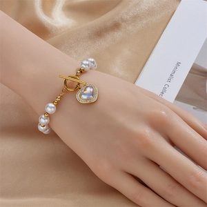 Detail eines Perlenarmbands mit goldenem Herzanhänger und Knebelverschluss am Handgelenk