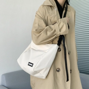 Model wearing a large white canvas messenger bag featuring minimalist fashion lettering