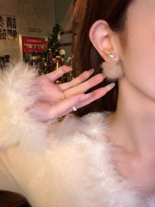Detail of elegant pearl earrings with beige plush balls worn on earlobe for winter style