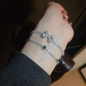 Close-up of a silver bow bracelet and a second chain featuring emerald green stones