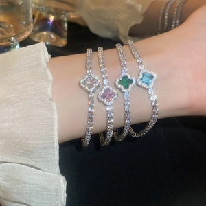 Close-up of four clover bracelets with sparkling zircons in pink, blue, and emerald tones