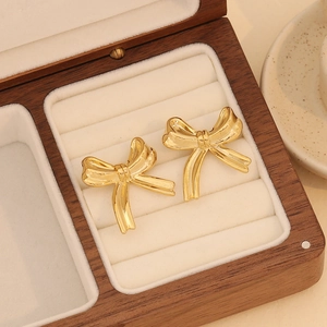 Golden bow stud earrings displayed in a luxury wooden jewelry box with beige lining