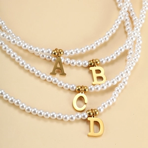Detail of elegant gold letter charms A B C D on white pearl necklaces with metallic luster
