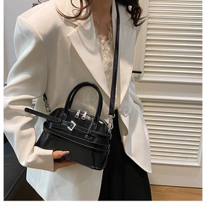 Detail of black glossy shell bag with wrap-around buckle and silver metal zippers