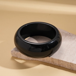 Detailed close-up of wide polished black stone bangle resting on a natural beige stone slab