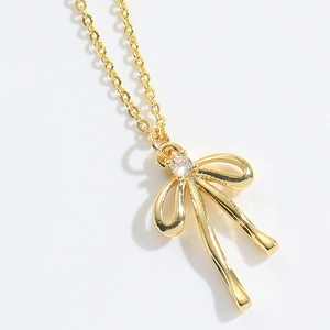 Detail of a gold bow pendant necklace featuring a white zircon stone on white background