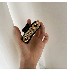 Detail of square hair claw clip featuring black base and golden chain link design