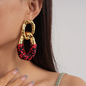 Close-up of oversized geometric earrings with gold metal and red-black textured wrap