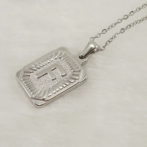 Detailed close-up of a silver stainless steel square pendant featuring an engraved letter F