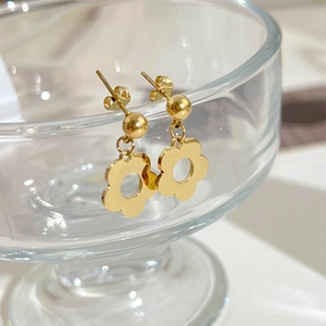 Elegant gold flower stud earrings hanging on a glass rim with a minimalist aesthetic