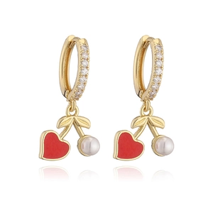 Close-up of gold cherry earrings with red heart charms and white pearls on white background