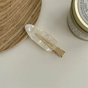 French style white resin hair clip with gold metal base on a minimalist wooden tray