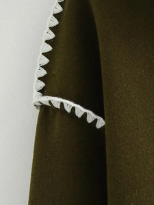 Detailed close-up of olive green wool coat with white zigzag decorative embroidery