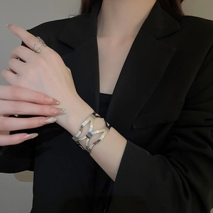 Macro detail of irregular silver cutout bracelet and matching ring on a black suit sleeve