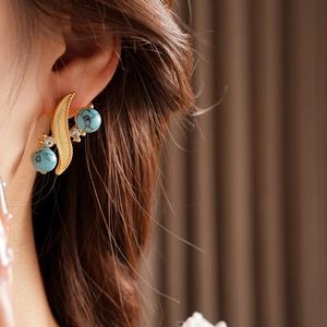 Macro side view of vintage gold S-shaped earrings with turquoise and diamonds on model