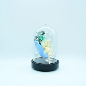 Close-up of preserved blue flower in a dome with glowing LED fairy lights and wooden base