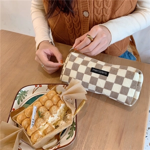 Brown and white checkered corduroy pencil case with a metal zipper on a wooden desk
