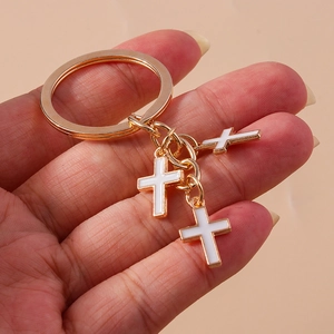 Detail of three white enamel cross charms hanging from a gold-tone metallic keychain