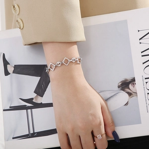 Detail of silver geometric link bracelet worn by model over a beige blazer background