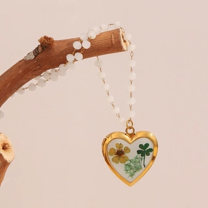 Detail of gold heart locket necklace with dried flowers on a branch branch