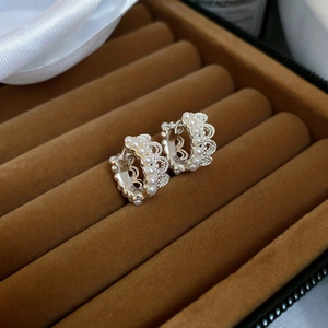 Close-up of white pearl earrings with silver lace crown design on brown velvet box