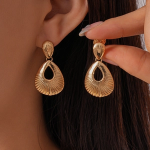 Detailed close-up of golden teardrop earrings with vintage texture on a model's ear