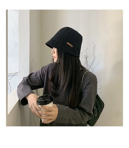 Close-up of black cotton bucket hat featuring a decorative brown handmade leather tag