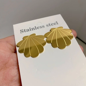 Detailed close-up of golden shell-shaped stainless steel earrings on a display card
